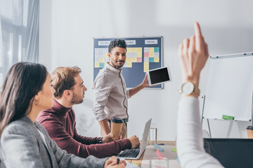 selective focus of bi-racial scrum master looking at businesswoman with raising hand