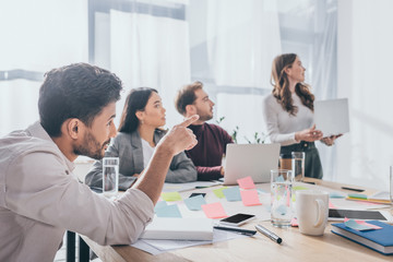 selective focus of mixed race scrum master pointing with finger near coworkers in office