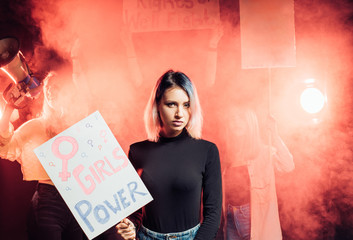 young caucasian female stand in the smoky space fighting for women power while people stand with posters in the background. feminists concept - obrazy, fototapety, plakaty