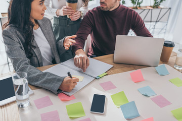 cropped view of businessman near asian businesswoman and coworker in office