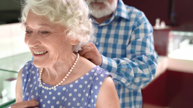 Happy mature man helping wife wearing pearl necklace at shop