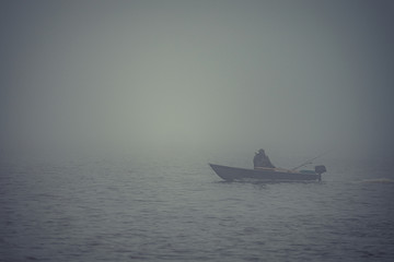 lonely fisherman on a boat, heavy fog on the lake