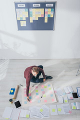 top view of scrum master holding marker pen near sticky notes while sitting on floor