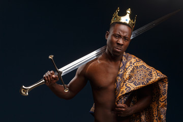 African man in a crown and cloak holds a sword in his hand.