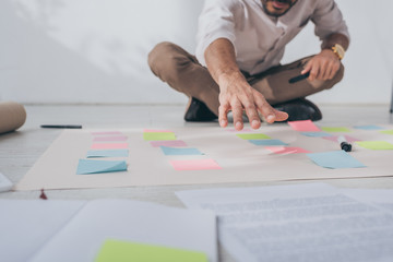 cropped view of mixed race businessman sitting with outstretched hand near sticky notes on floor