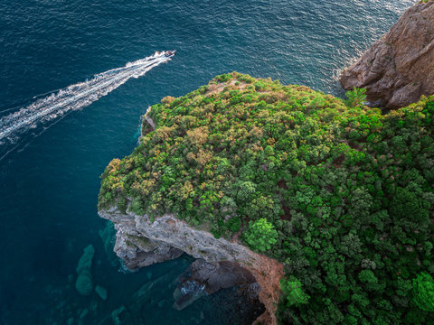 Aerial view of a steep cliff and a motor boat. Jagged coast on the Adriatic Sea. Cliffs overlooking the transparent sea. Wild nature and Mediterranean maquis © Naeblys