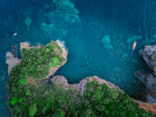 Aerial view of a steep cliff and a motor boat. Jagged coast on the Adriatic Sea. Cliffs overlooking the transparent sea. Wild nature and Mediterranean maquis