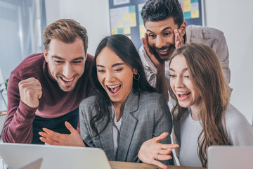 smiling multicultural businesswomen and businessmen looking at laptop in office