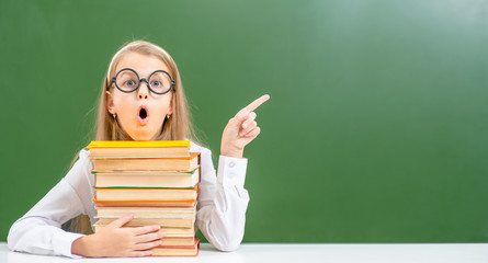 Surprised girl with books points on empty chalk board. Empty space for text