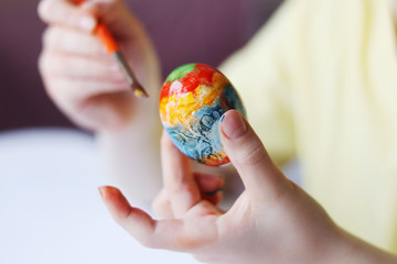 Child painting eggs with paints on Easter holiday
