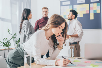 selective focus of pensive scrum master holding pen near coworkers