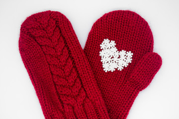 Close up of a knitted red mitten with white snowflakes in the shape of a heart on a white background, isolated. Сoncept of Christmas, winter, love, care and Valentine's day