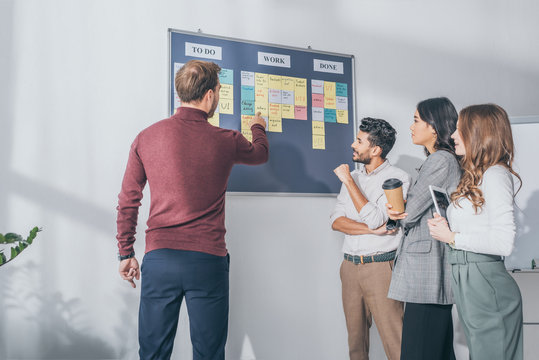 back view of scrum master pointing with finger at board with letters near multicultural coworkers