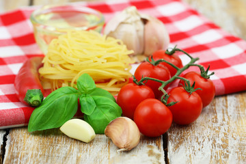 Ingredients for cooking pasta: tagliatelle, cherry tomatoes, garlic, fresh basil, chili and bowl of olive oil on checkered cloth