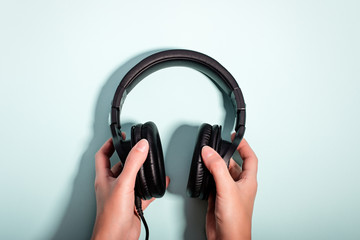 Black massive headphones in female hand on pastel background, copy space. Modern technology flat...