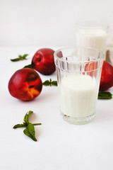 Two glasses of milk or kefir, fresh whole peaches and sprigs of basil on a white textile tablecloth. The concept of proper nutrition with dietary foods high in protein and vitamins