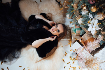 Girl in a dress lies in the Christmas scenery. Fashionable young woman wearing luxurious evening...