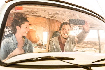 Indie couple ready for roadtrip on oldtimer mini van transport - Travel lifestyle concept with young hippie people having fun traveling on minivan adventure trip - Warm bright filter