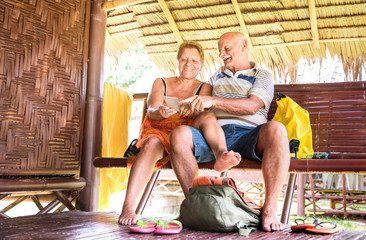 Fototapeta na wymiar Happy senior couple using mobile smart phone at bungalow luxury resort - Active elderly and travel concept always connected with new trends and technology at adventure trip around world - Warm filter
