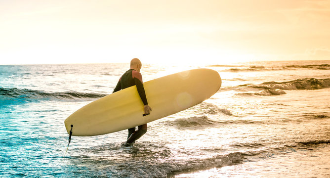 Lonely surfer walking with longboard at sunset in Tenerife - Surfing adventure lifestyle and sport travel concept - Multicolored sunshine filtered tones