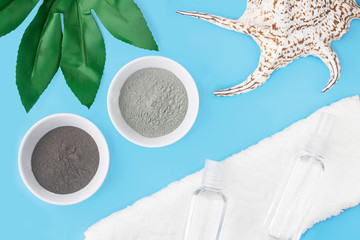 Cosmetic clay on a blue background, next to a towel, sea shell, and tropical plant. The concept of...