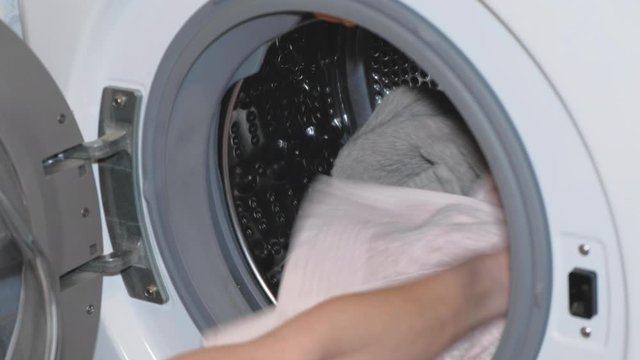 Woman housewife puts clothing in the washing machine close up