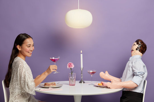 Asian woman forgets about real relationship problems, clinks glass of cocktail, flirts with imaginary man, pretends feeling love to mannequin, gets ready for date. Perfect relations simulation