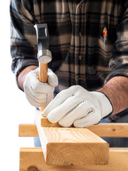 Close-up. Carpenter with his hands protected by gloves, with hammer and nails fixes a wooden board. Construction industry, do it yourself. White background.