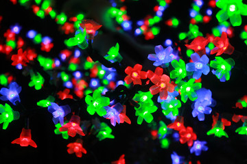 Colorful light bulbs in the form of flowers. A shining tree of multicolored flowers. A bright garland, light bulbs. Festive evening illumination, flickering lights, illumination.