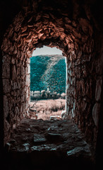 Stone window in an old fortress in pocitelj, view of the distant mountain hill. Creepy eerie mood, artistic image, teal and orange tones