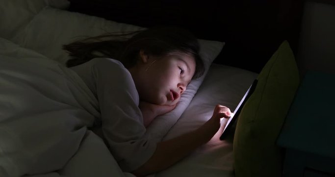 Face Lit Of Six Years Old Girl Typing On Smart Phone Lying On Bed At Night  