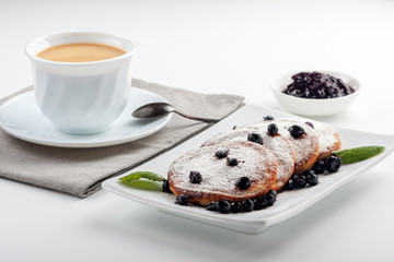 A Cup of coffee with milk and a plate with a pancakes is on the table.