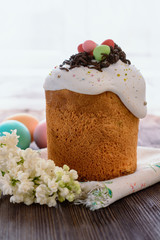 Easter cake next to colored eggs and a sprig of blooming lilac