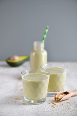 Smoothie or yogurt made from avocado and almond in a glass and a bottle. Light background, copy space, vertical.