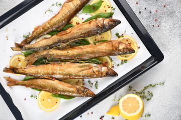 Whole fish, fried or smoked, on a baking sheet with lemon and herbs. Top view.