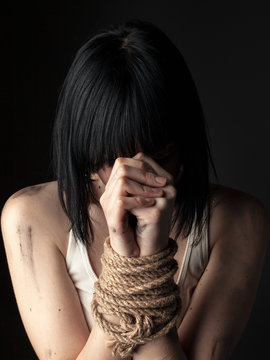 Portrait of  young woman with bound hands on black background.