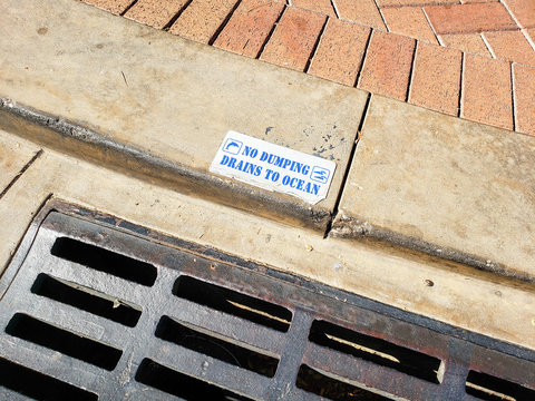 Looking Down At A Storm Drain Along The Street, Featuring A Sign That Says No Dumping Drains To Ocean.