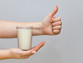 A woman's hand holds in the open palm a glass of fresh milk against a white background. minimalism. The concept of healthy dairy products with calcium. Sign class
