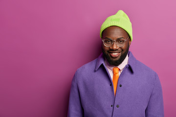 Happy dark skinned male entrepreneur dressed in bright stylish clothes, smiles pleasantly, being in...
