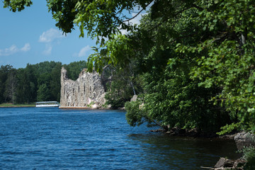 ancient historical ruins on the water's edge; blue river water, there are big trees all around. Sunny day with blue sky.