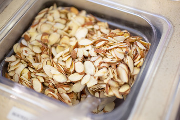 A closeup view of a container of sliced almonds in an ice cream shop setting.