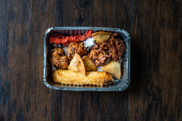 Take Away Indian Food Plate with Chicken Pakora, Aloo Tikki, Samosas Samsa and Spring Rolls in Plastic Container Box / Package.