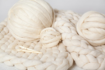 a ball of thick yarn and wooden needles lie on a blanket of Merino wool