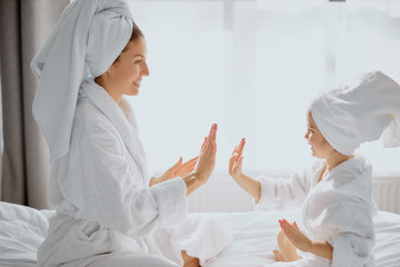 caucasian woman and little child daughter sit playing game of clapping hands together, friendly family