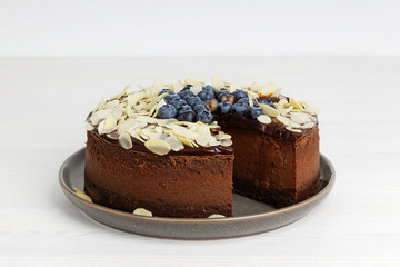 Closeup homemade chocolate cheesecake with blueberries and almond slices on white wooden table. Copy space.