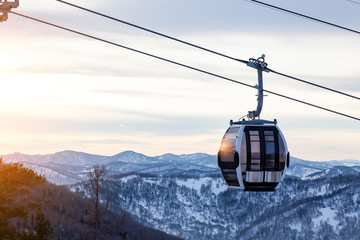 Cabin of a gondola cableway suspended on a rope where sits people with skis and snowboards high in the Altai mountains with snow and blue sky on winter sunset. Ski resorts and snowboarding. © Aleksandr Kondratov