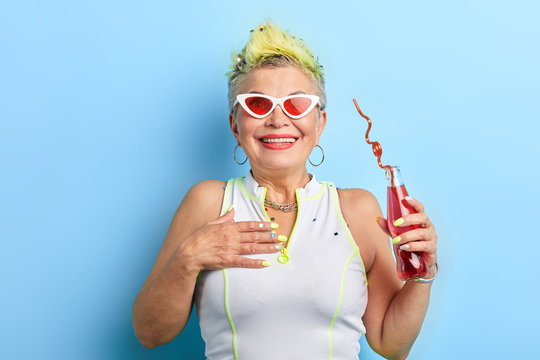 romantic cool old lady with palm on her breast in sunglasses drinking juice and posing to the camera. holiday concept. free time, spare time, leisure