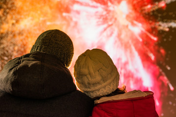 Merry man and woman in the winter clothes during fireworks at night.
