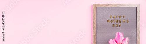 Mother's day greetings on letter board and beautiful tulips on pink trendy monochrome backdrop. Web banner