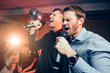 two young caucasian men in t-shirts singing in microphone in karaoke bar, having fun, celebrating....